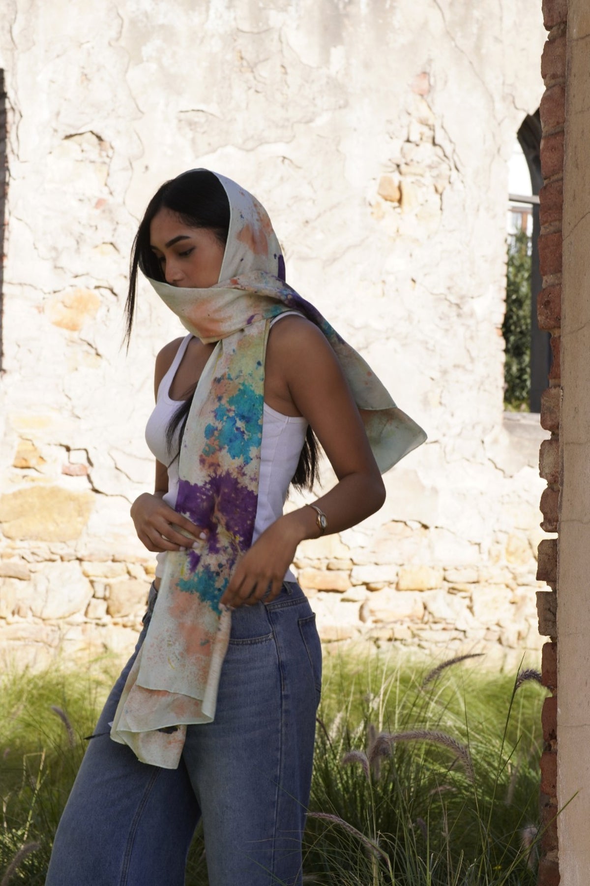 Hand-painted silk wrap worn as a headscarf and draped around a woman, featuring an abstract multicolour design.