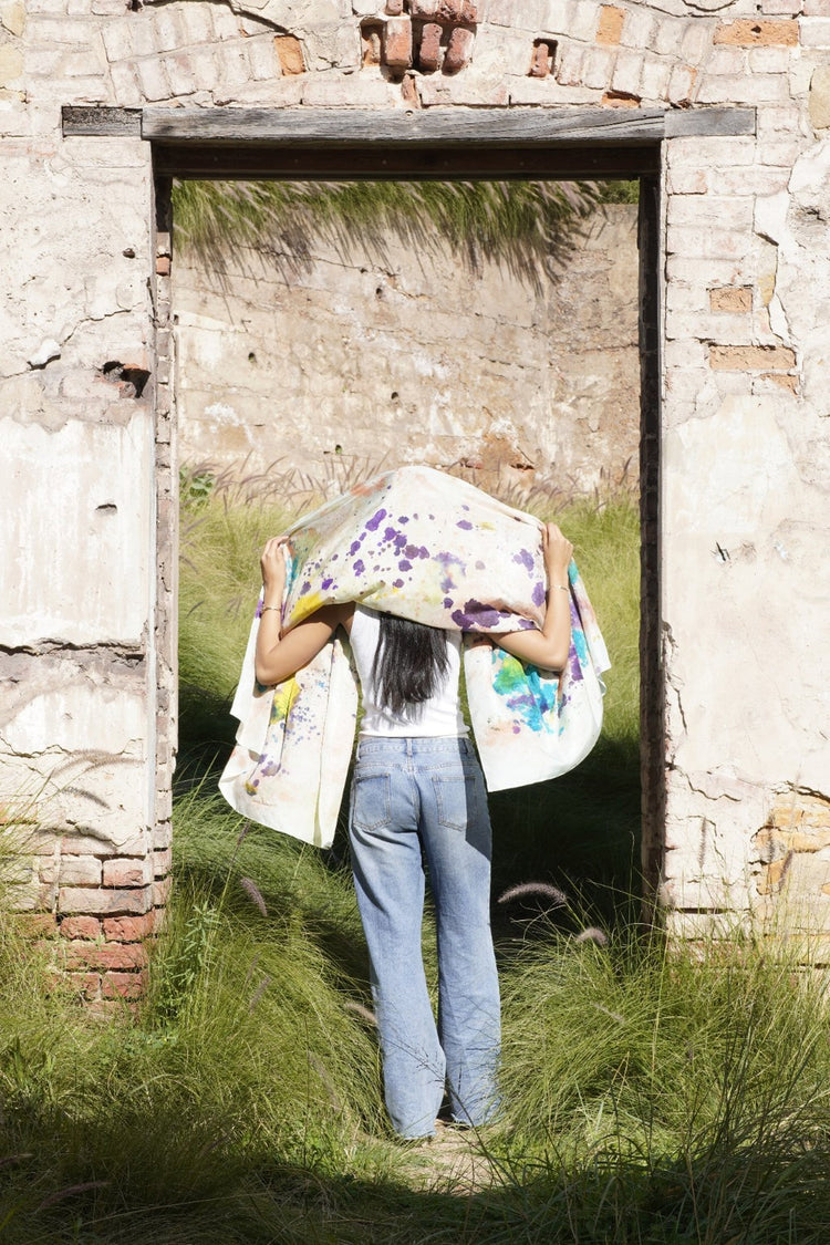 Hand-painted silk wrap draped beautifully as a headscarf around a woman standing in a brick doorway, featuring an abstract multicolour design.
