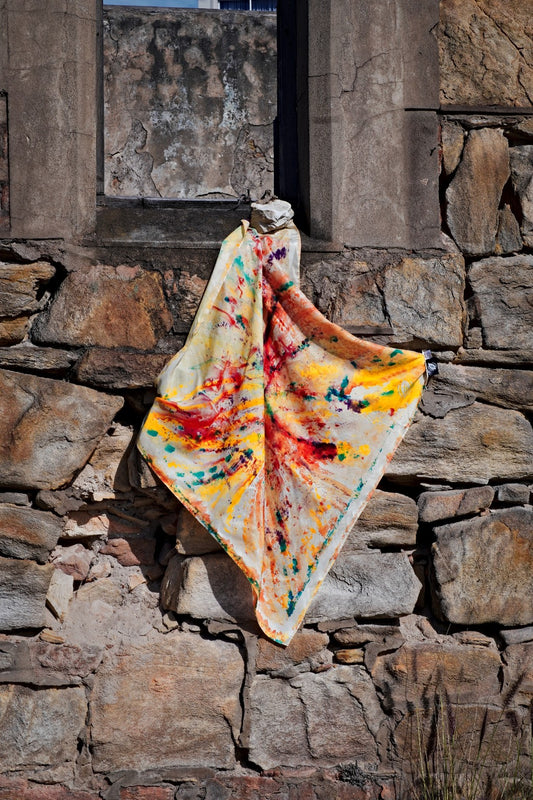 Hand-painted silk scarf draped on a brick wall with vibrant multicolours red, yellow, blue and brown