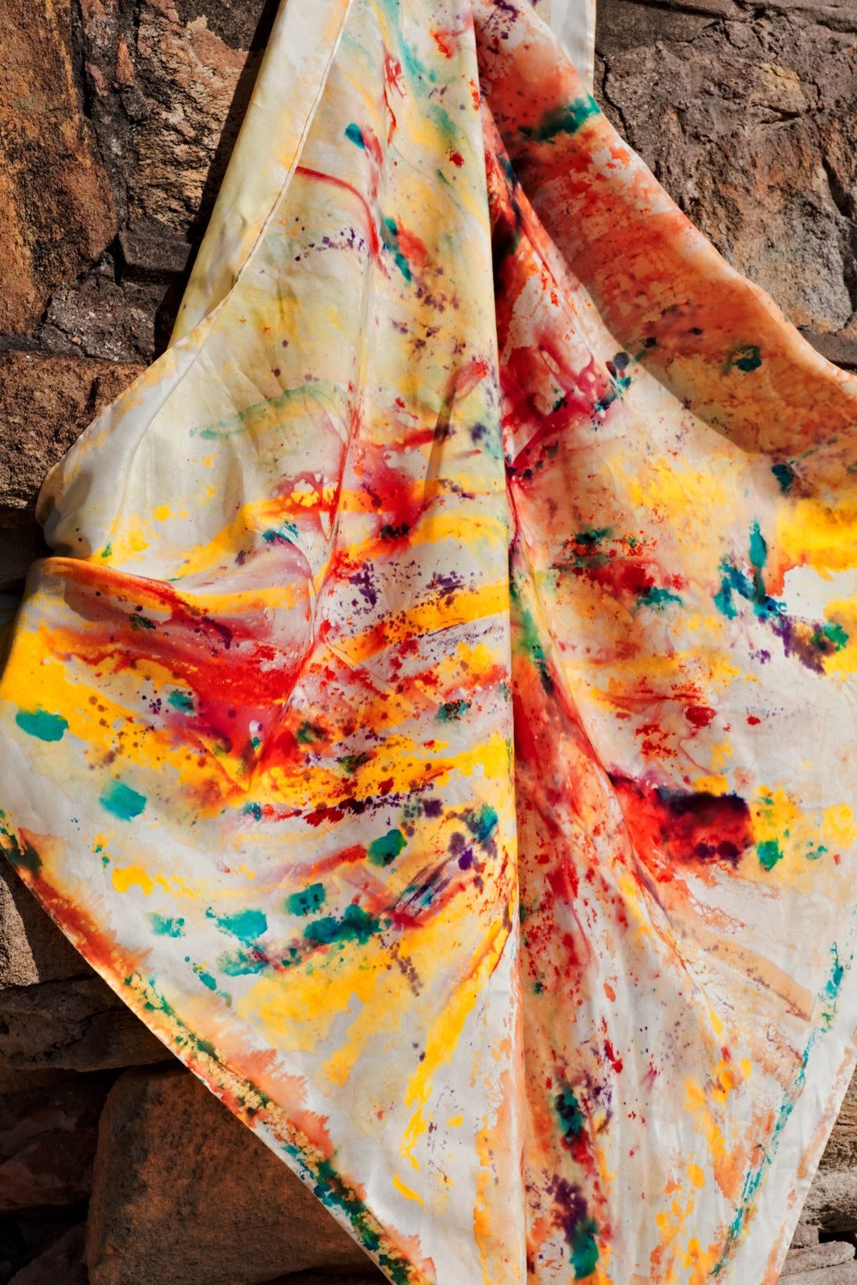 Close up of hand-painted silk scarf draped on a brick wall with vibrant multicolours red, yellow, blue and brown