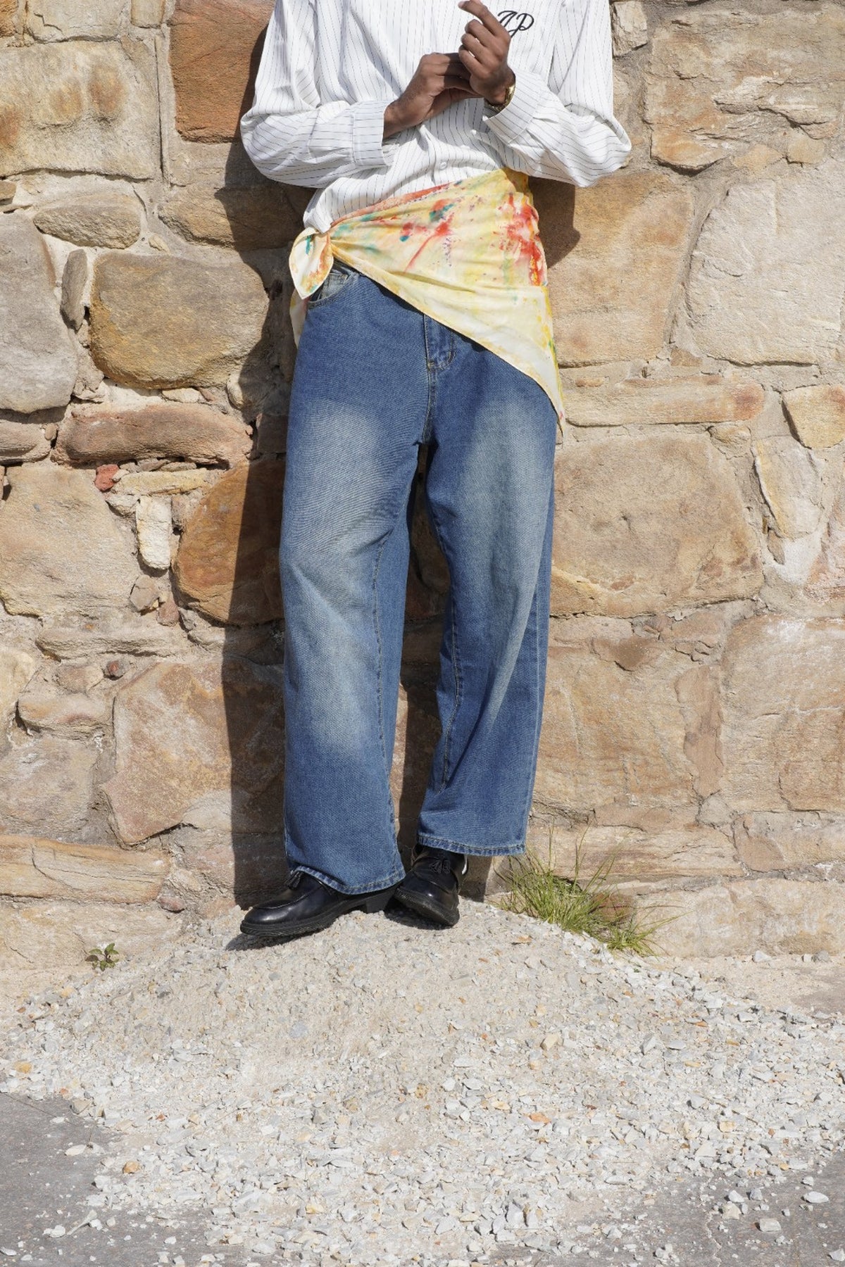 Hand-painted silk scarf worn around the waist by a man, photographed against a rustic stone and brick setting.