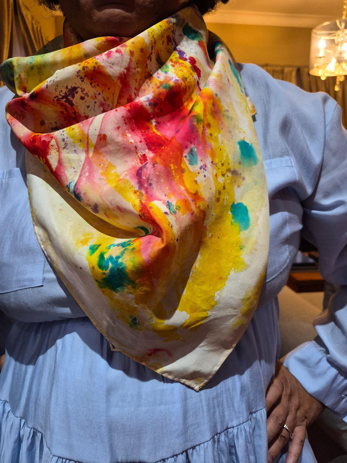 Close-up of a hand-painted silk scarf draped around the neck of a woman, in yellow, orange and green.