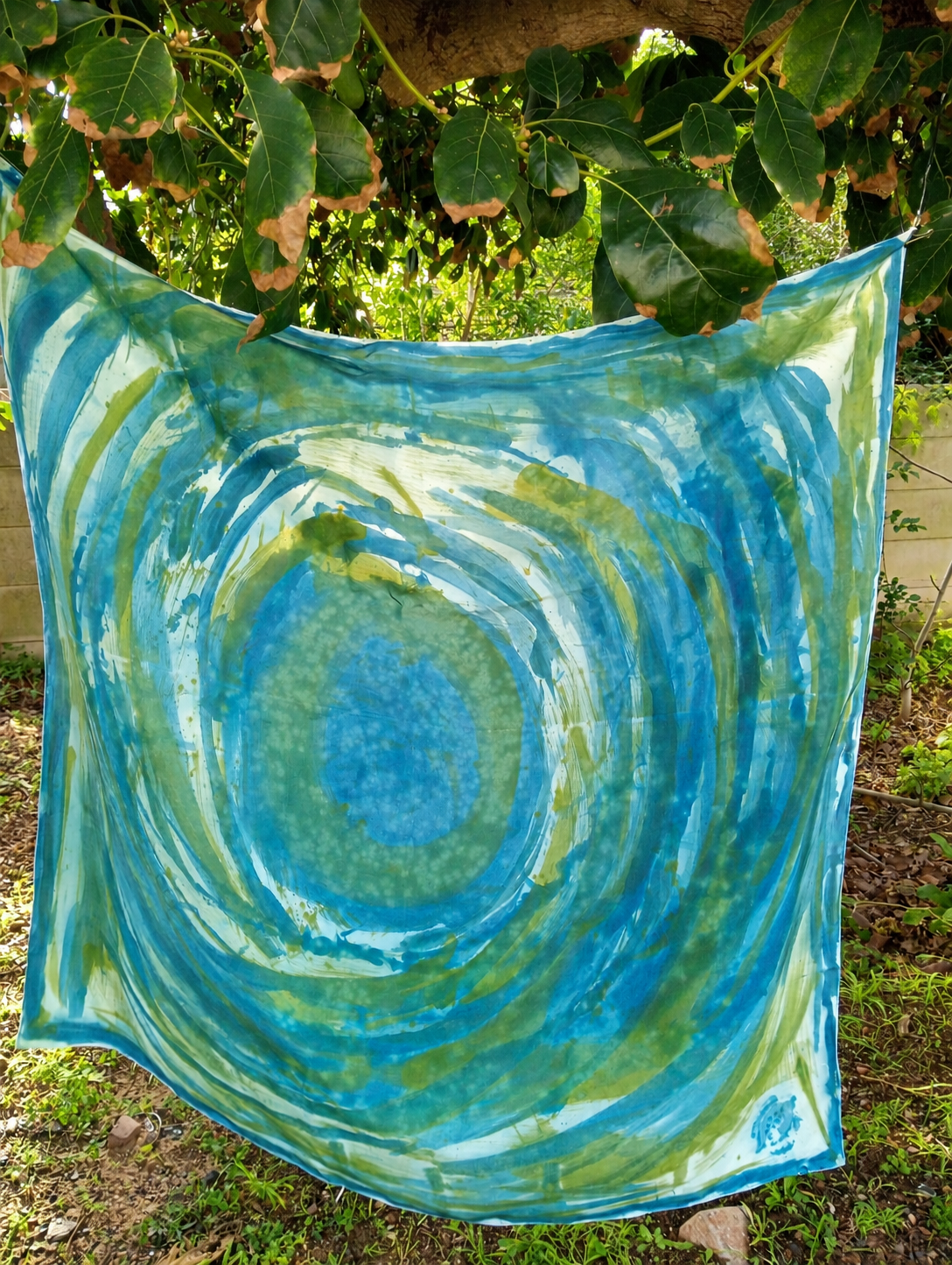 Hand-painted Mulberry silk scarf in blue, green and white with concentric abstract brushstrokes, displayed outdoors beneath tree branches.