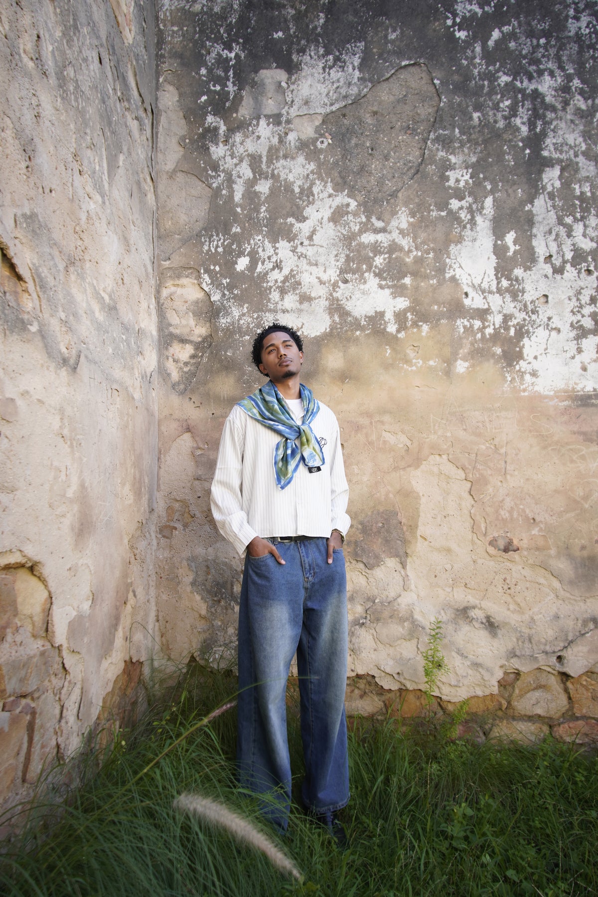 Hand-painted Mulberry silk scarf worn by a man, featuring a blue and green abstract pattern, photographed against a weathered stone wall.