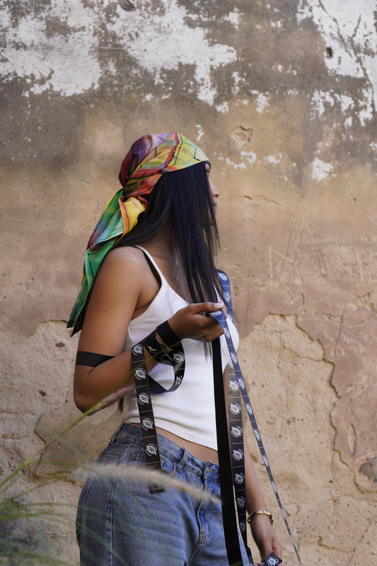 Woman wearing a colourful hand-painted Mulberry silk scarf as a headscarf, standing outdoors against a weathered wall.